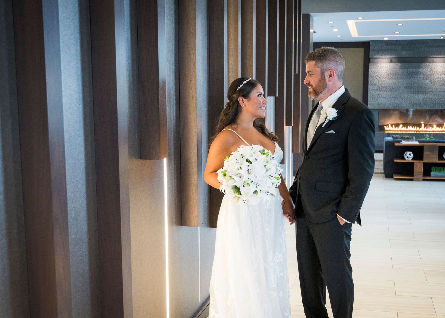 A bride and groom share an intimate moment in a modern hallway with sleek lighting and reflective surfaces.