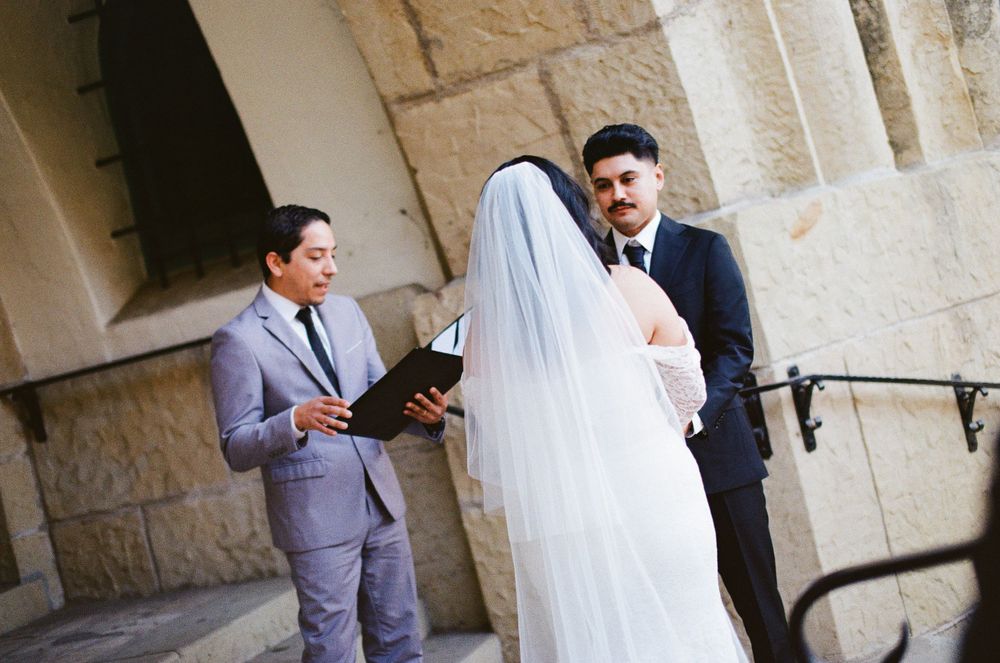 An eloping couple standing on the exterior stone staircase (Area F) of the Santa Barbara Courthouse, styled with editorial 35mm film wedding
