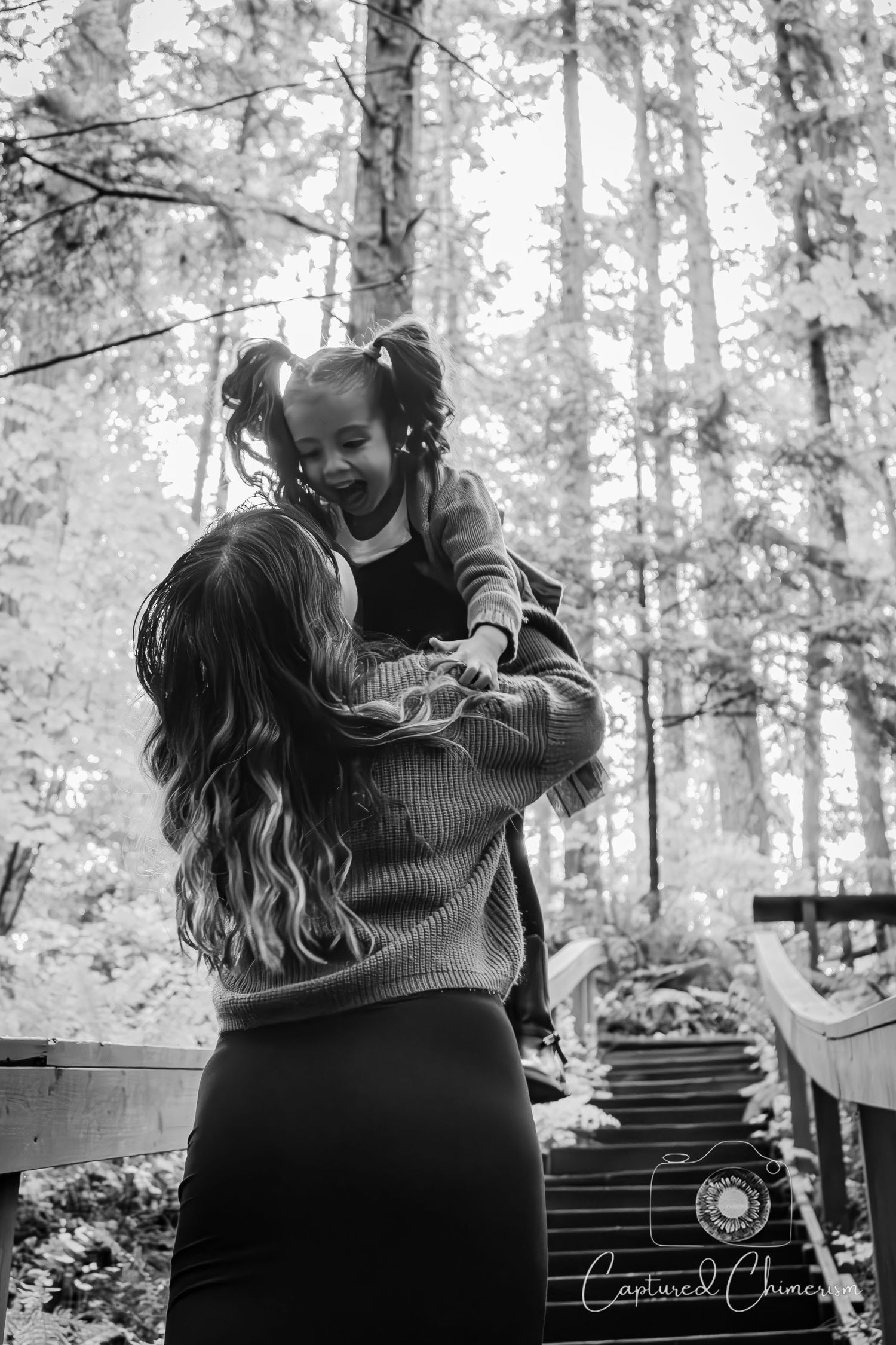 Black and white portrait of tender outdoor moment between parent and child in a forest setting.