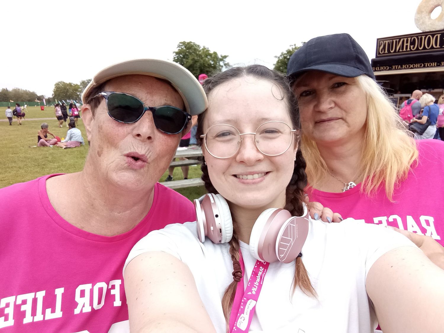 Group wearing pink shirts and hats smiles together at outdoor event in sunny weather.