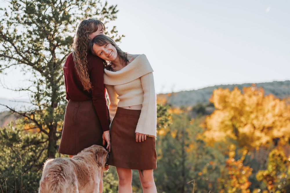 Two people in warm fall clothing embrace while standing on a rocky overlook with autumn foliage in the background.