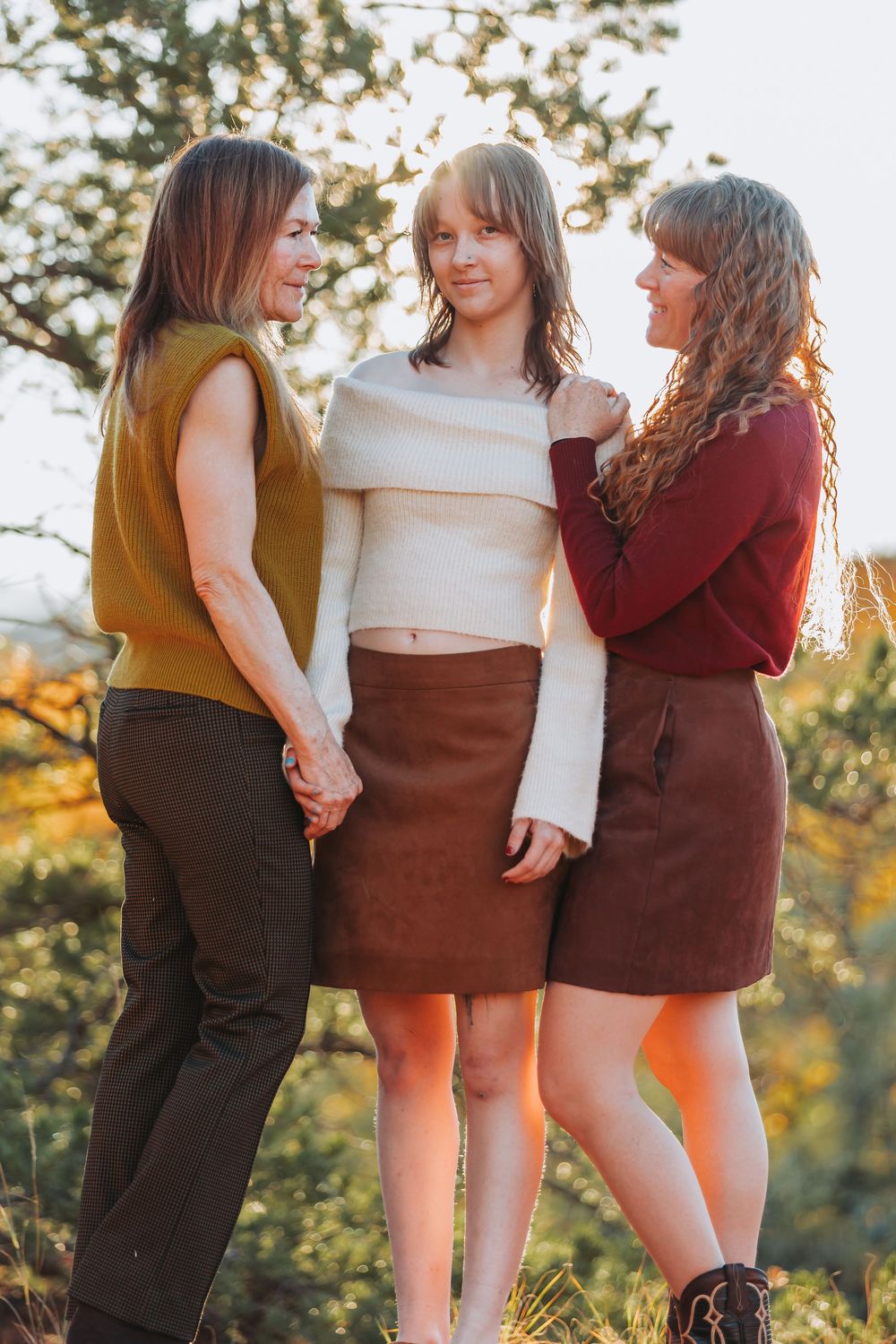 Three friends in autumn colors share a candid moment together at golden hour in an outdoor setting.