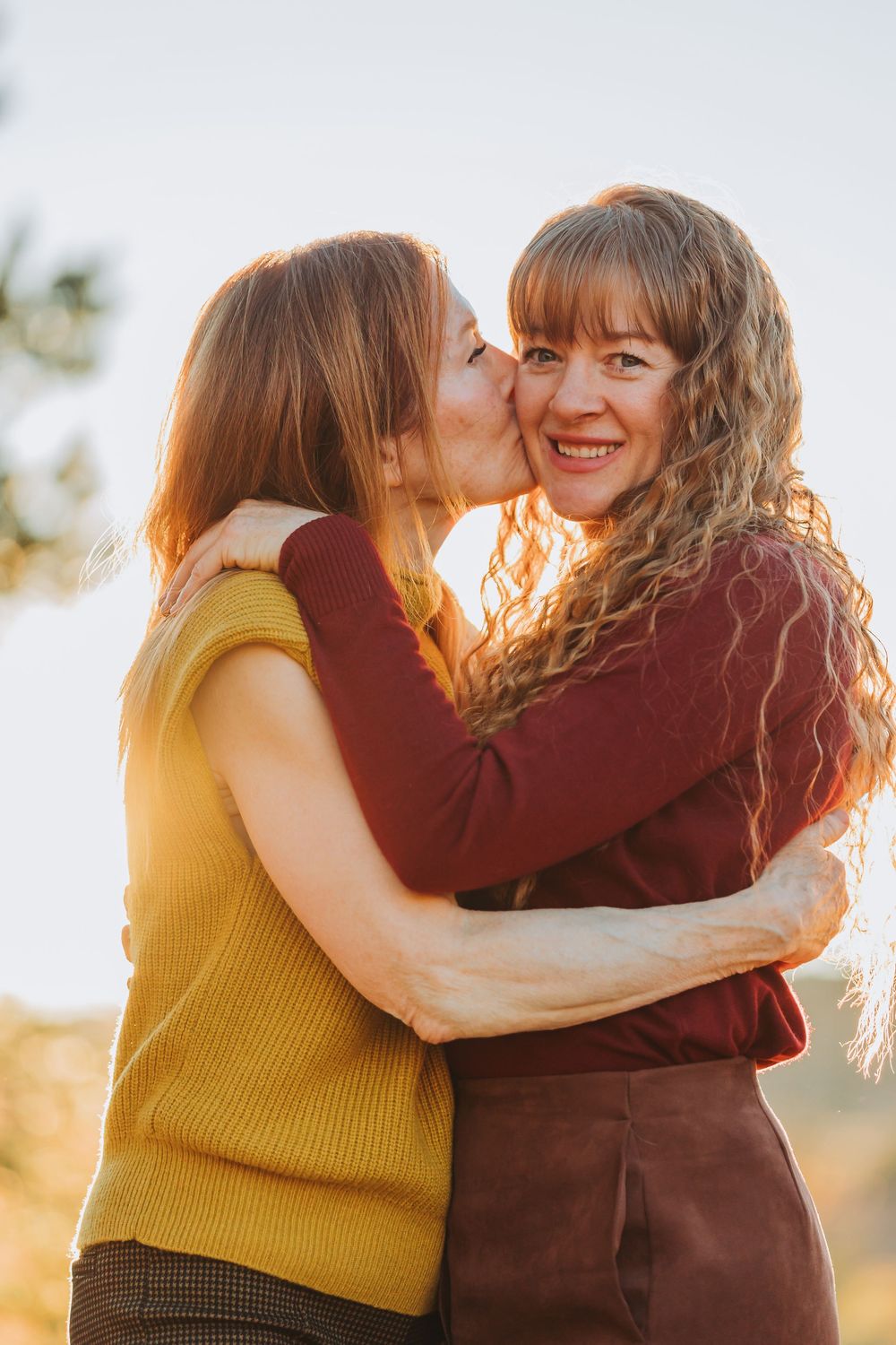 Two friends share an affectionate moment while embracing during sunset with warm golden lighting.