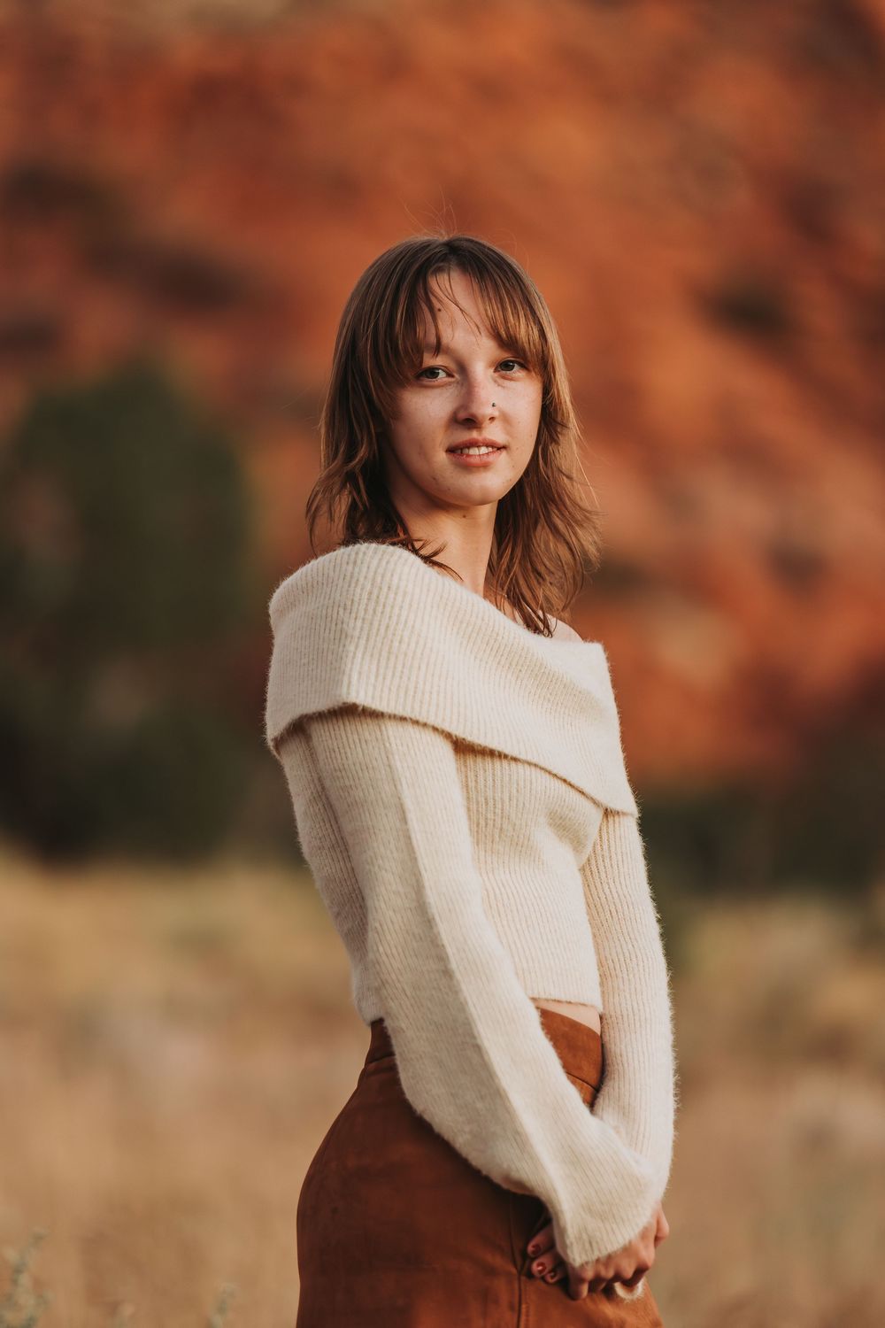 Person in cream sweater poses against warm autumn background with red rock formations in desert landscape.