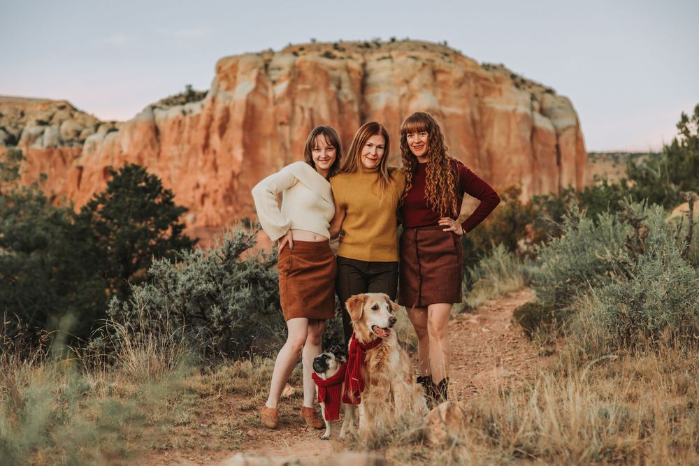 A group poses together against red rock formations in a desert landscape during golden hour.