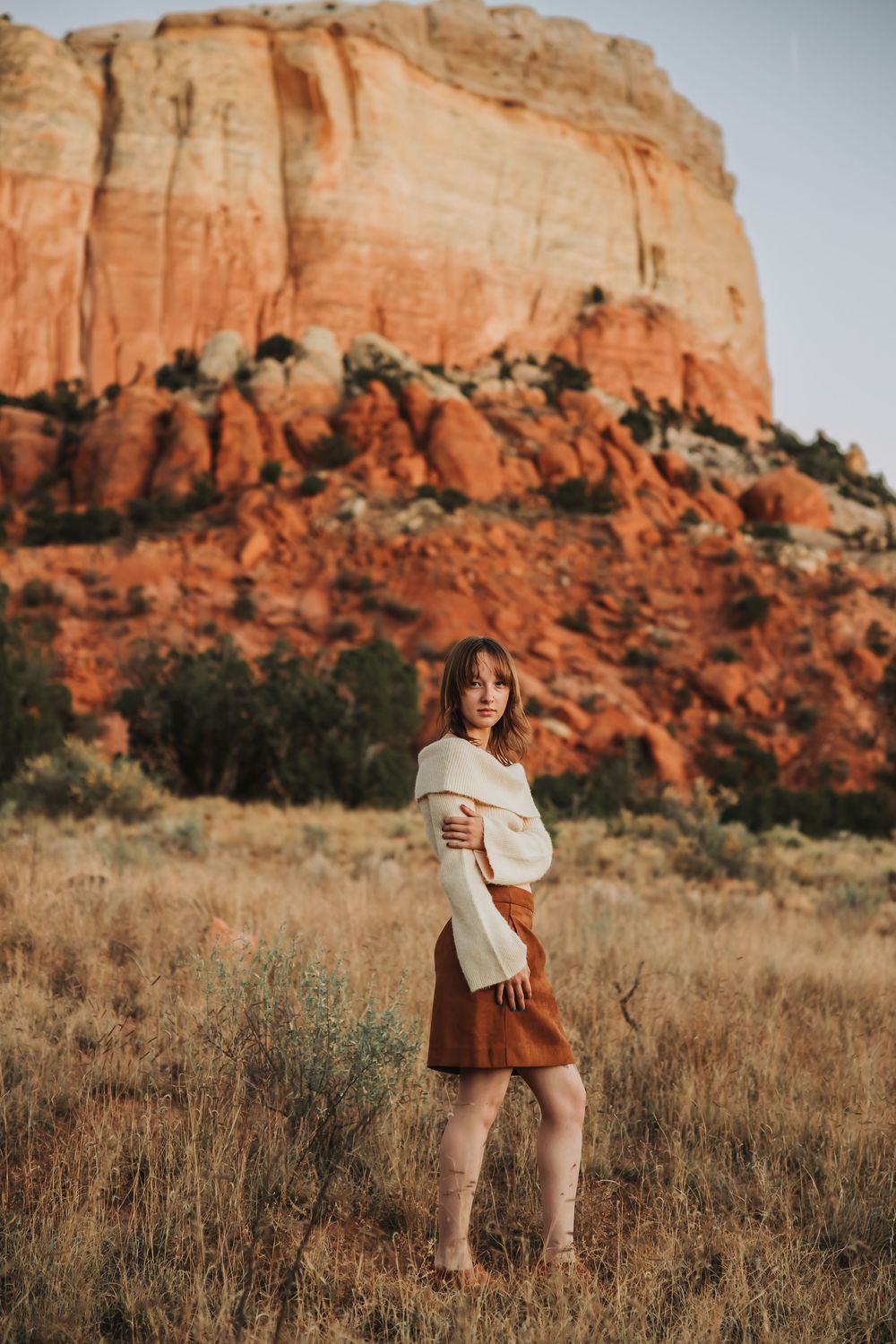 A scenic desert landscape with red rock formations and desert brush in the foreground at sunset.