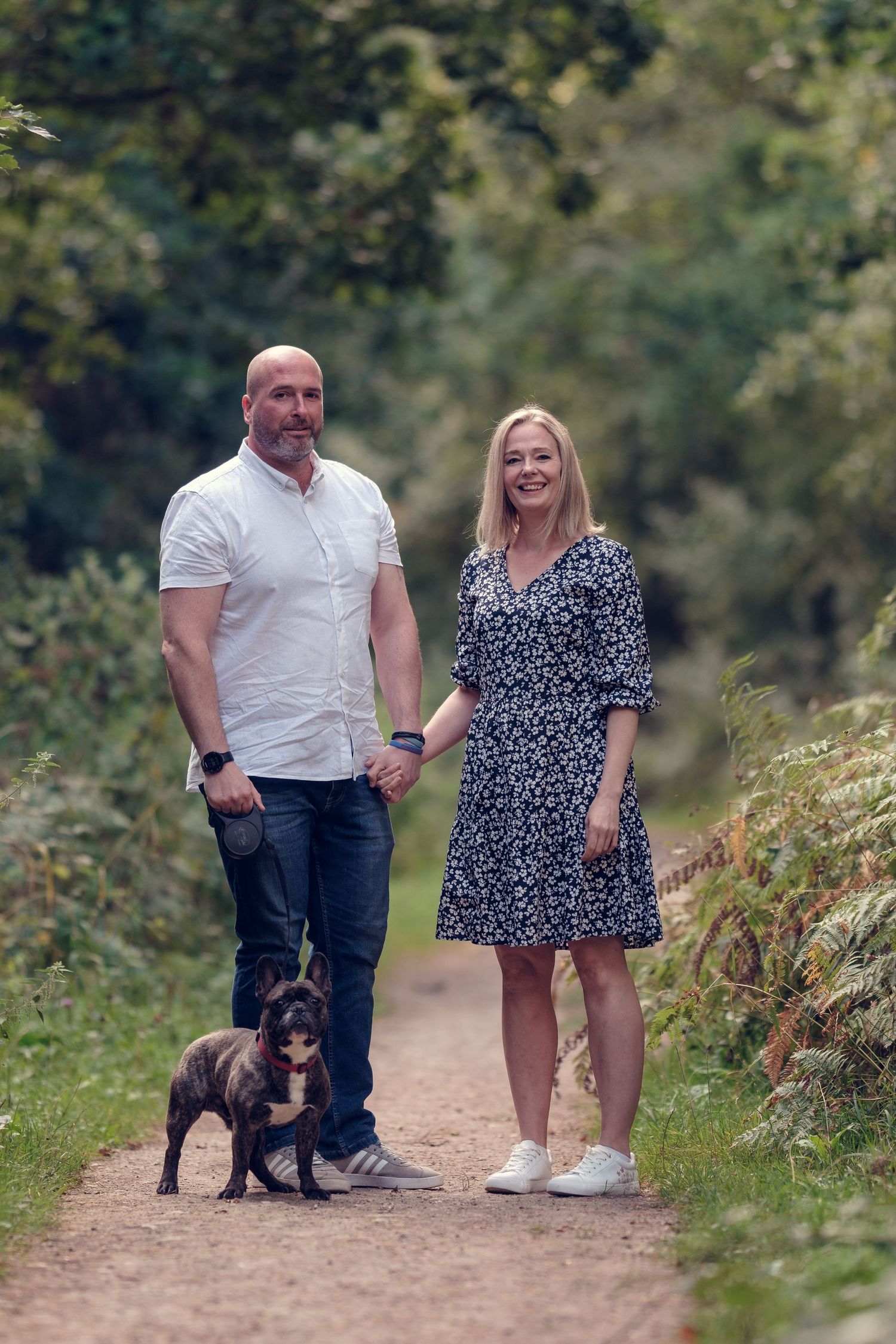 A couple walks along a nature trail with their small black dog on a sunny afternoon.
