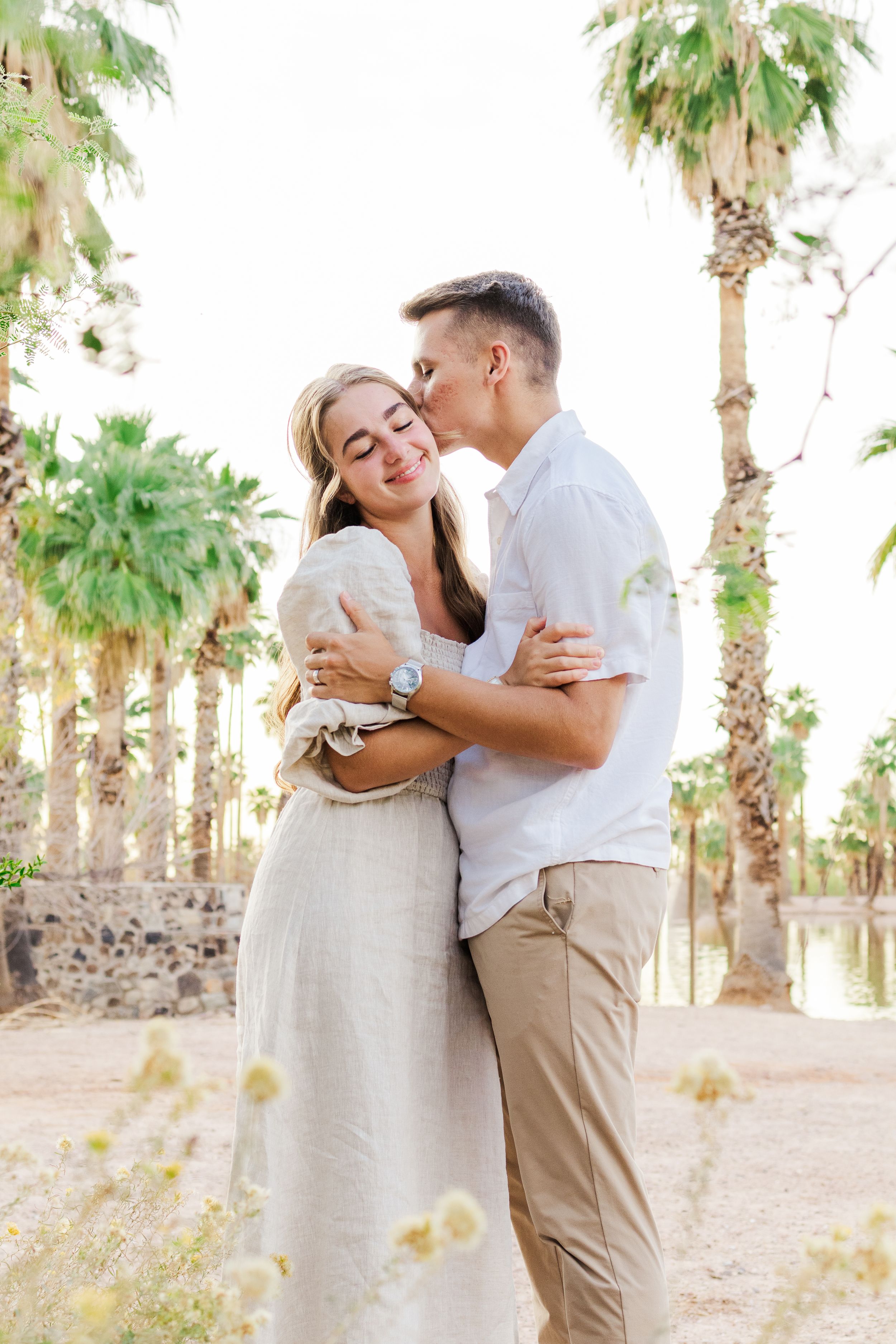 Light & airy image of a young married couple hugging with dry grass in the foreground and palm trees in the background at Papago Park.