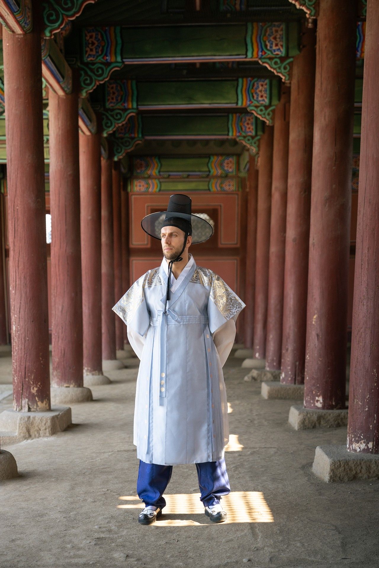 Traditional Korean figures in hanbok stand under wooden pillars at Gyeongbokgung Palace in Seoul.