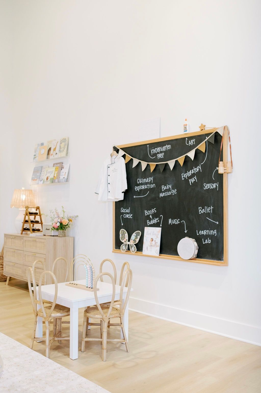 Modern minimalist room with white table, wooden chairs, chalkboard wall decor advertising the bunny hive class programming in natural light.