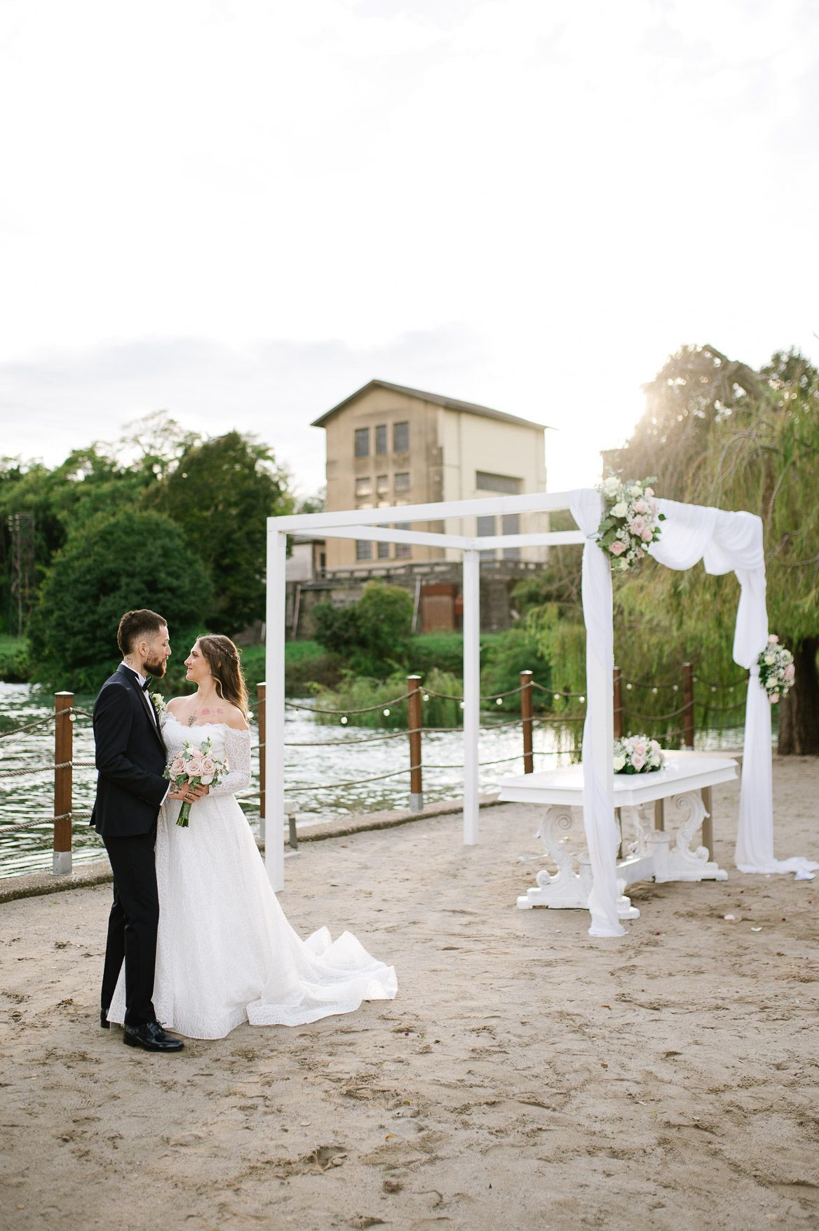 A romantic beach wedding ceremony setup with white pillars and flowing fabric creating an elegant aisle on the sand.