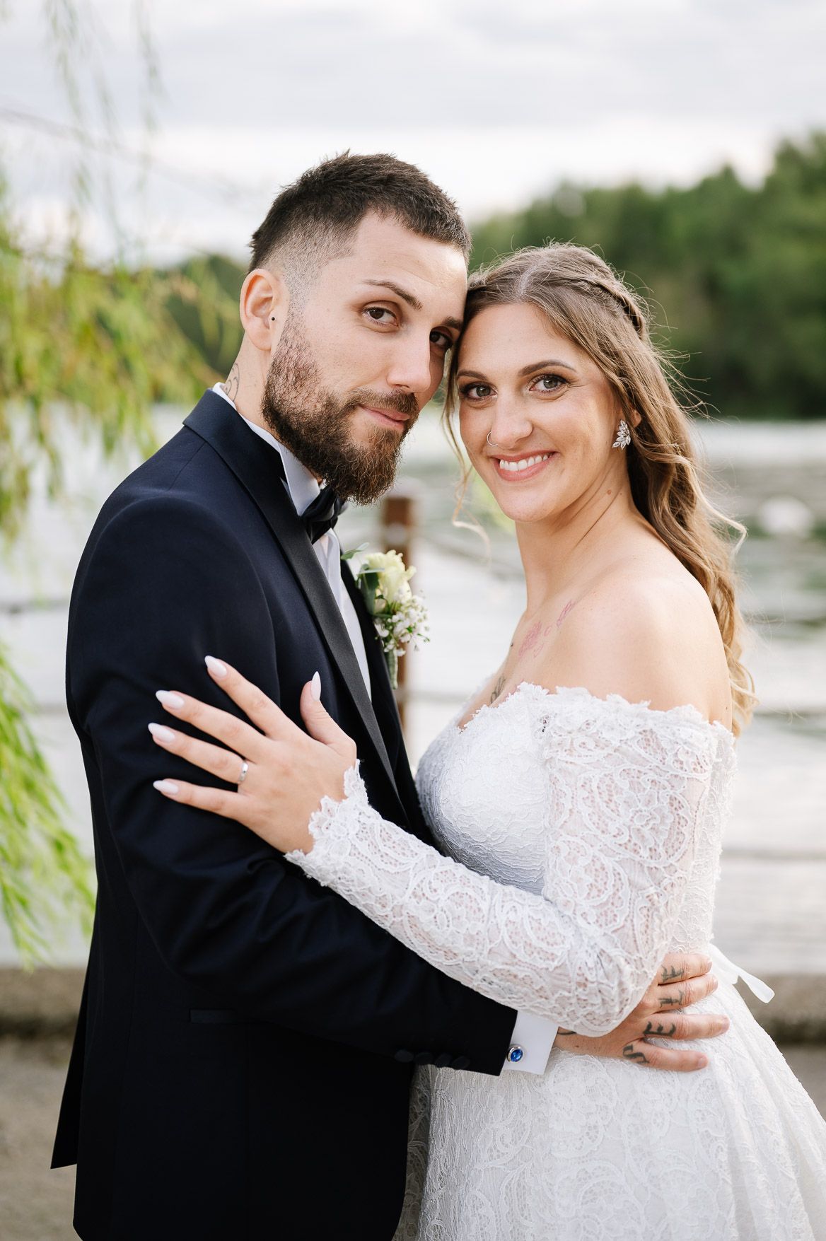 Romantic wedding couple embraces outdoors in elegant black tuxedo and white lace gown.
