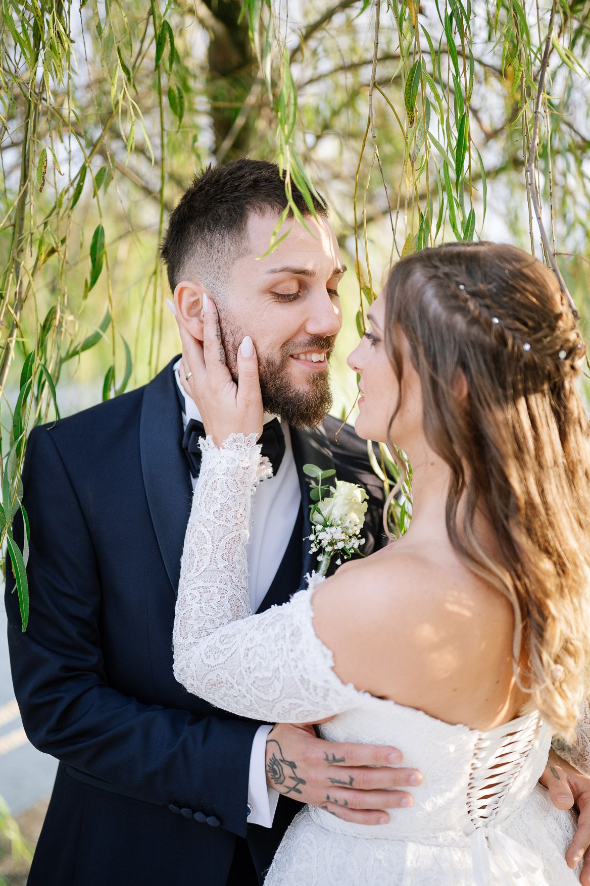 Wedding couple shares tender moments beneath drooping willow branches in a garden setting.