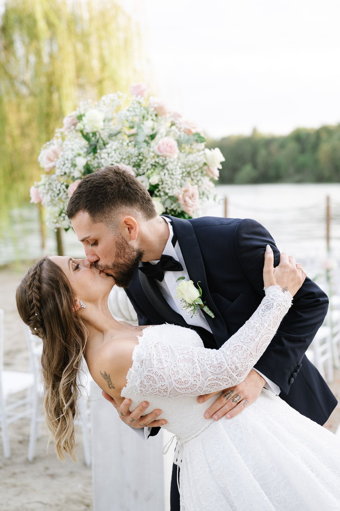 Romantic wedding couple shares intimate dance poses beneath willow trees by the water.
