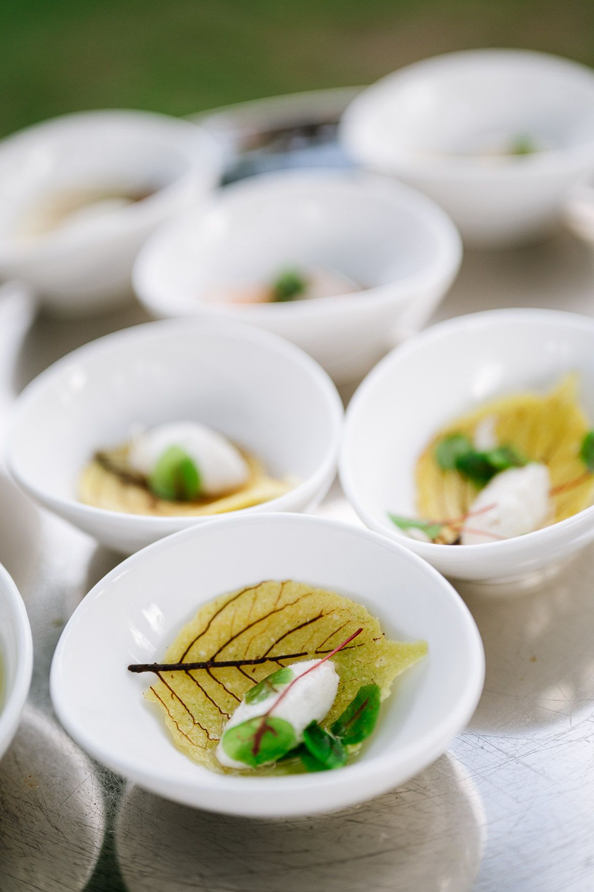 Elegant white ceramic spoons with delicate garnishes and sauces arranged in a row for fine dining presentation.
