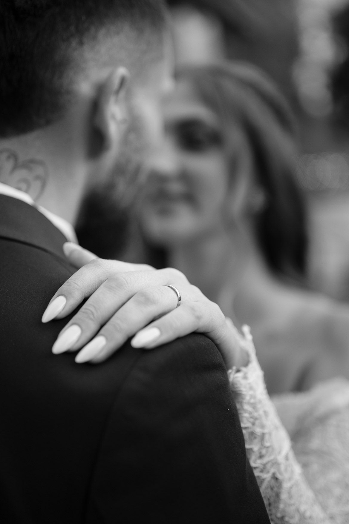 A close-up shot of hands resting on a shoulder during a formal wedding ceremony.