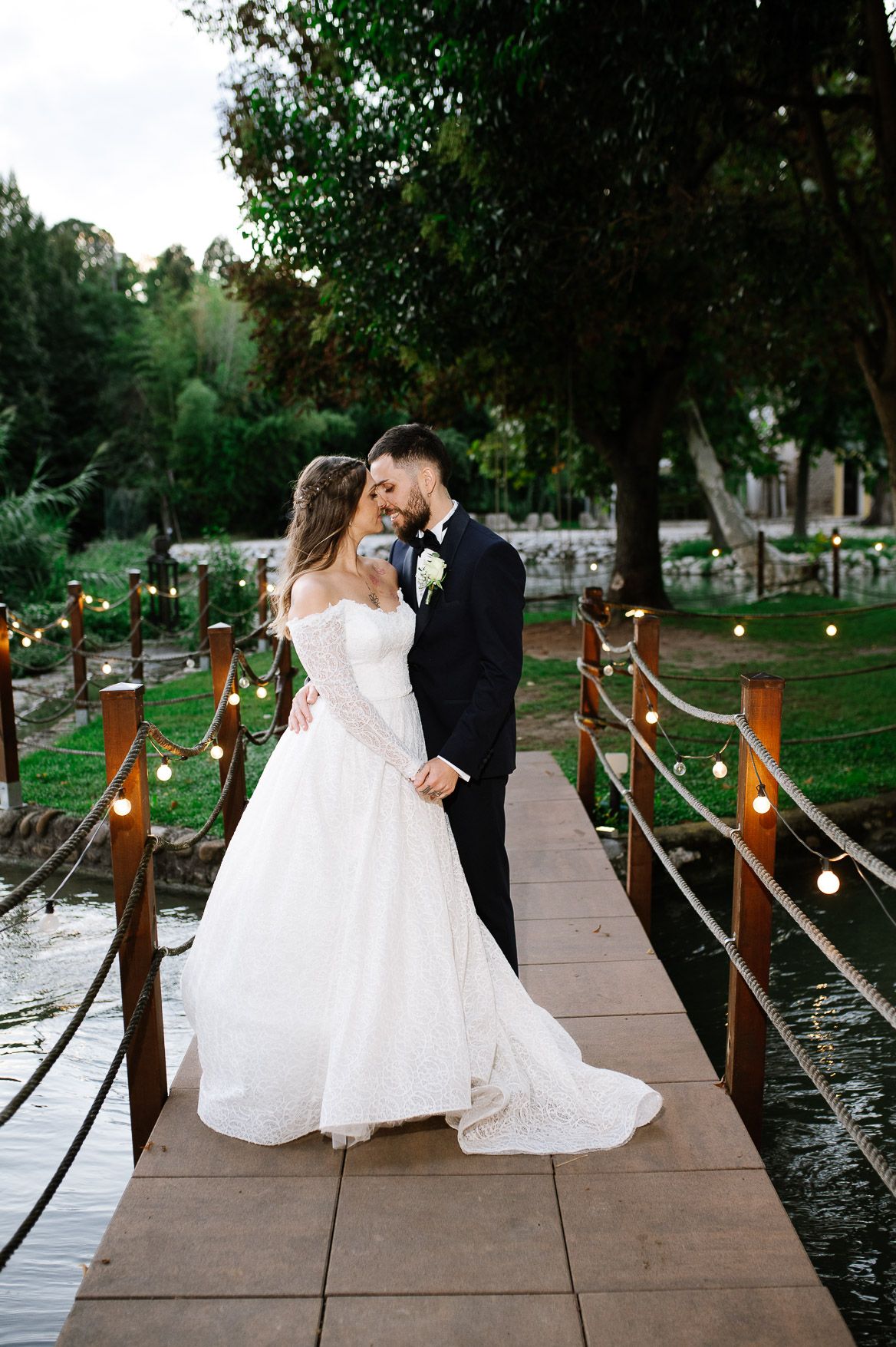 Wedding couple poses on wooden dock decorated with string lights at sunset.