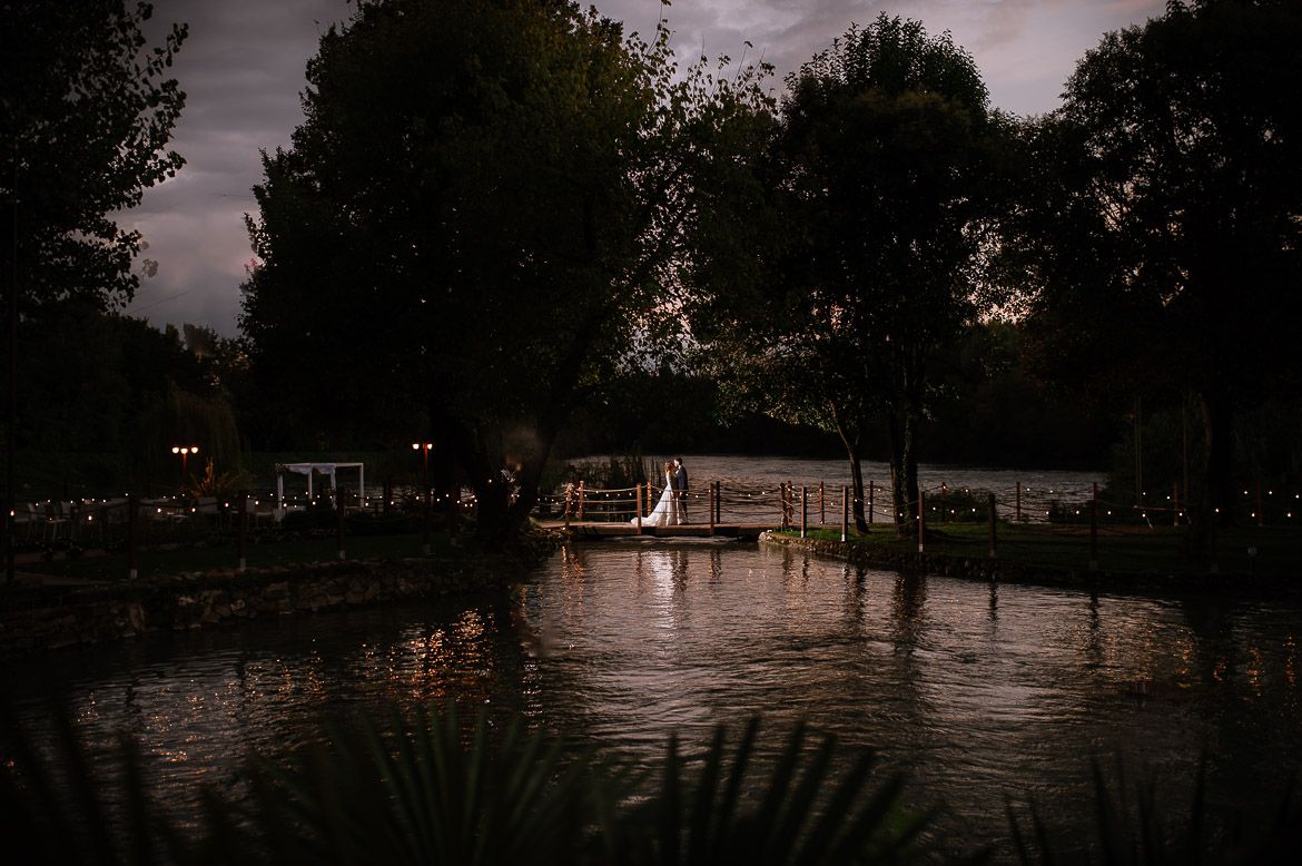 Panoramic twilight landscape showing silhouettes of trees against a dusky sky over water.