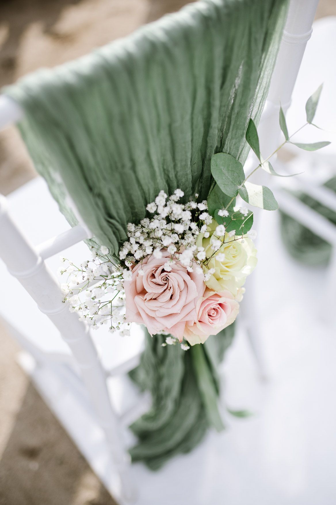 Elegant wedding chair decor featuring sage green fabric and delicate pink roses with baby's breath.