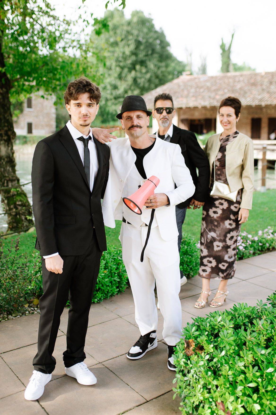 Wedding party members in black and white formal attire pose casually along a garden walkway.