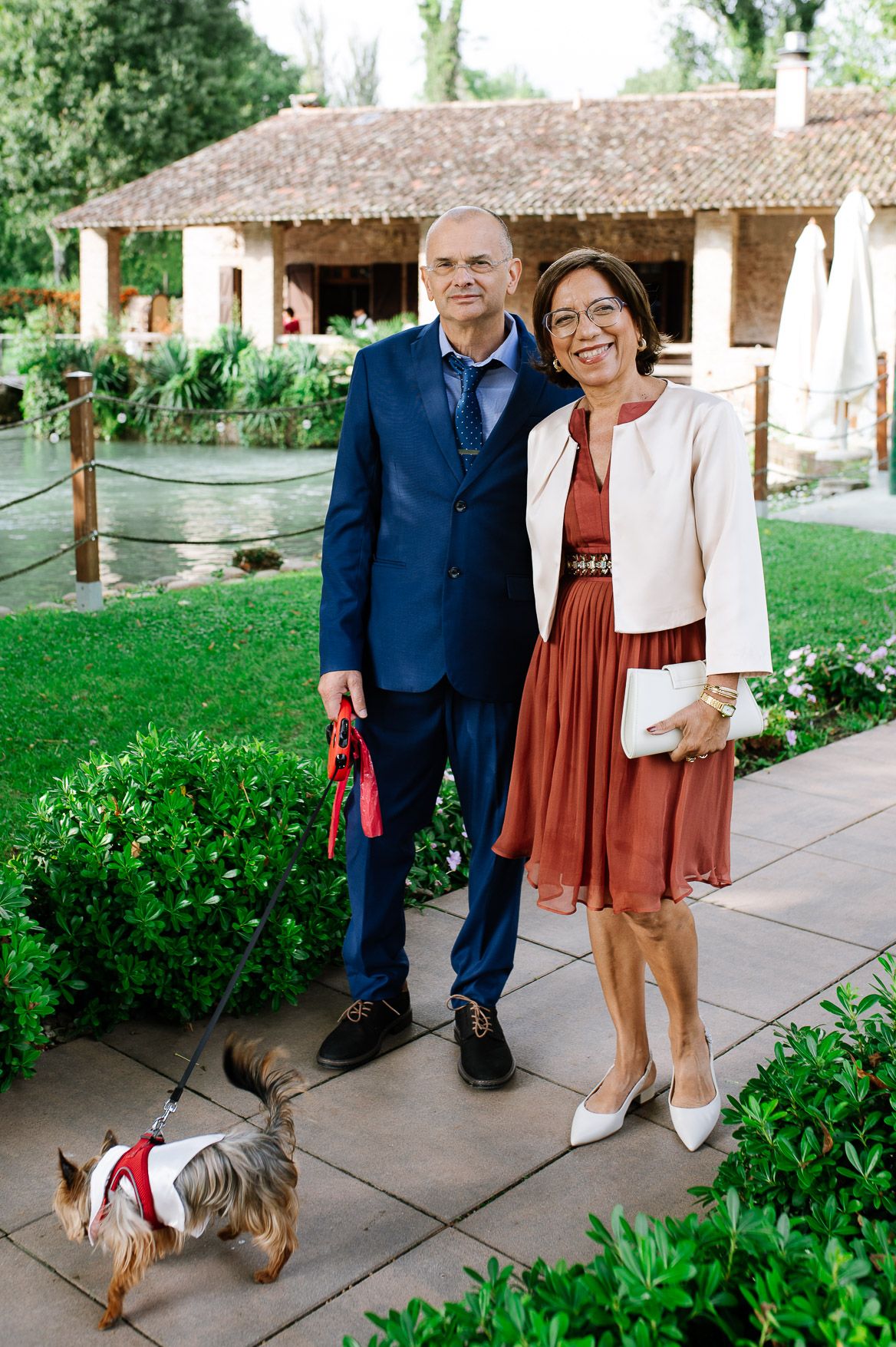 Couple strolling together on garden path with woman in rust-colored dress and man in navy suit.