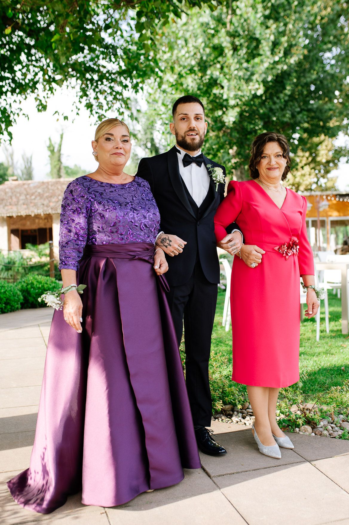 Wedding party poses on garden path wearing formal attire in purple and red tones.