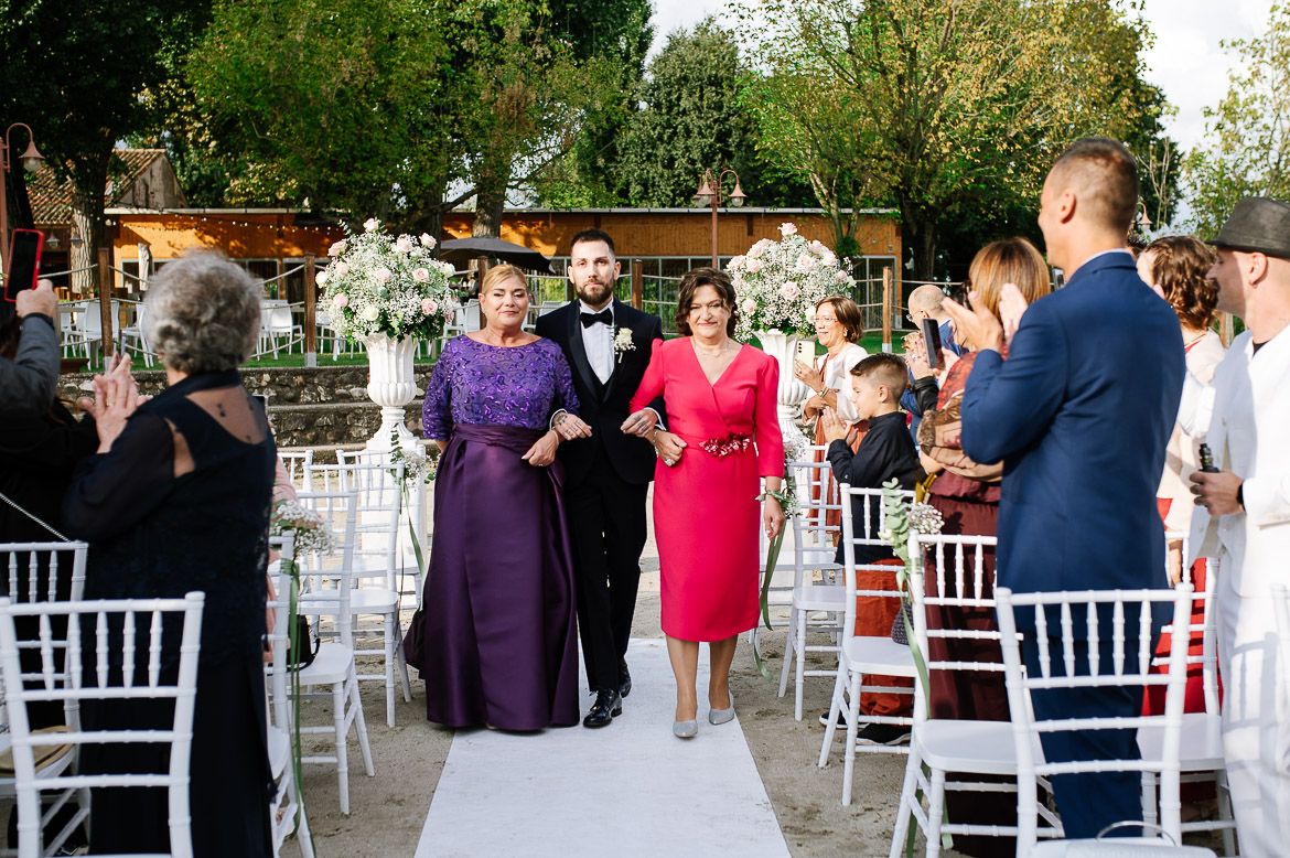 White chairs arranged in rows for an outdoor wedding ceremony with guests mingling.