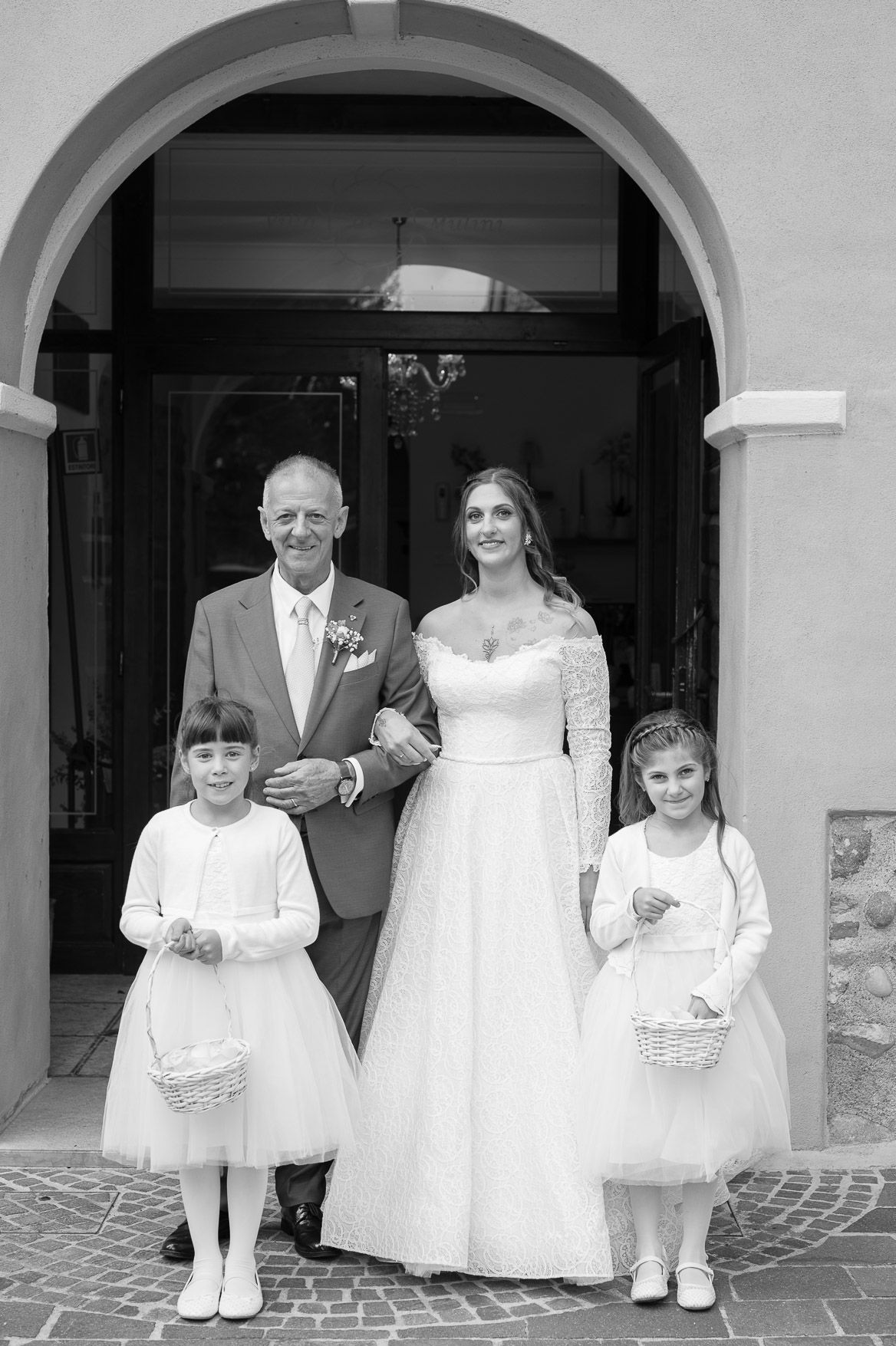 A series of five black and white wedding photos showing people in formal attire under arched doorways.