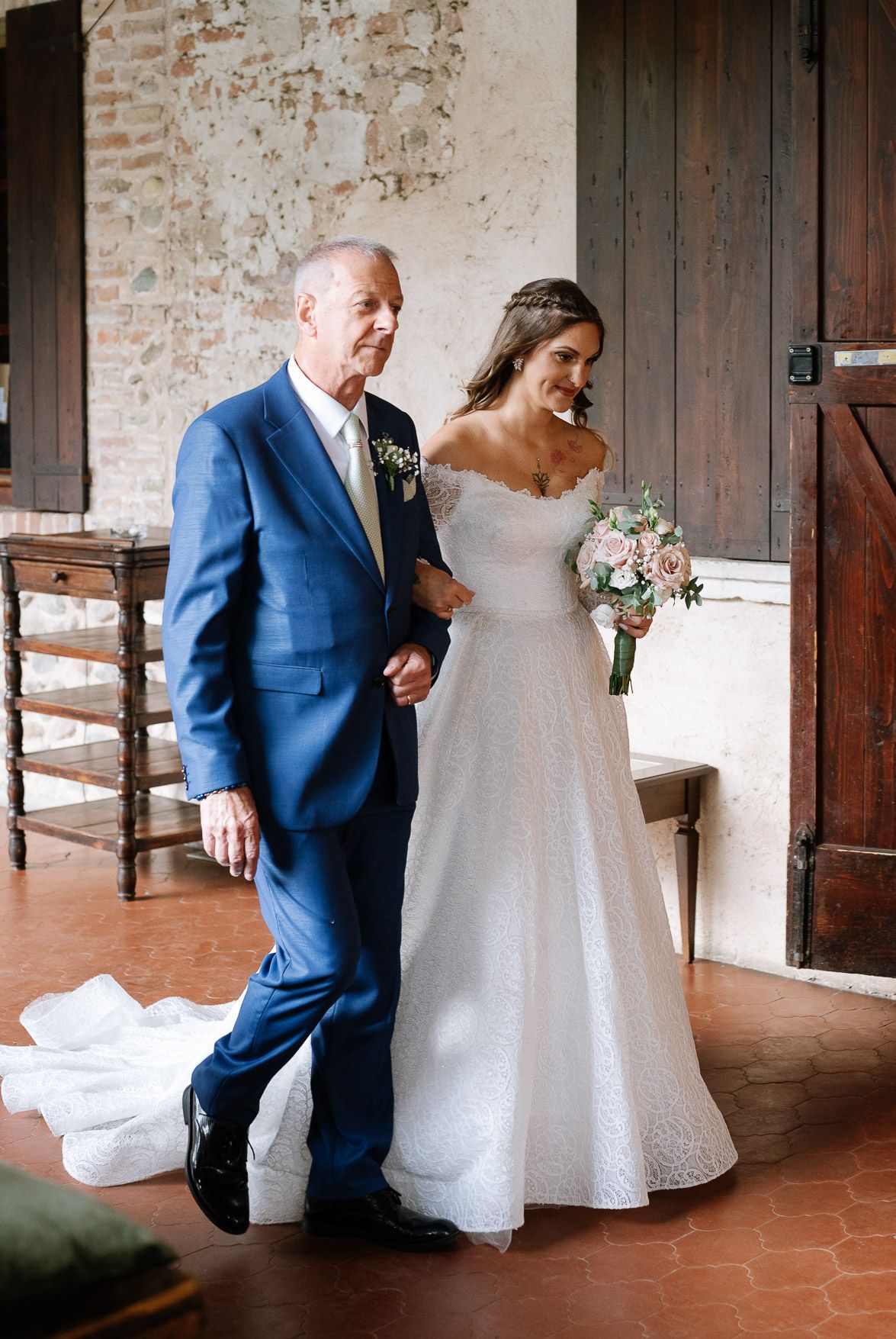 First look moments captured in a rustic brick corridor with blue suit and white wedding dress.