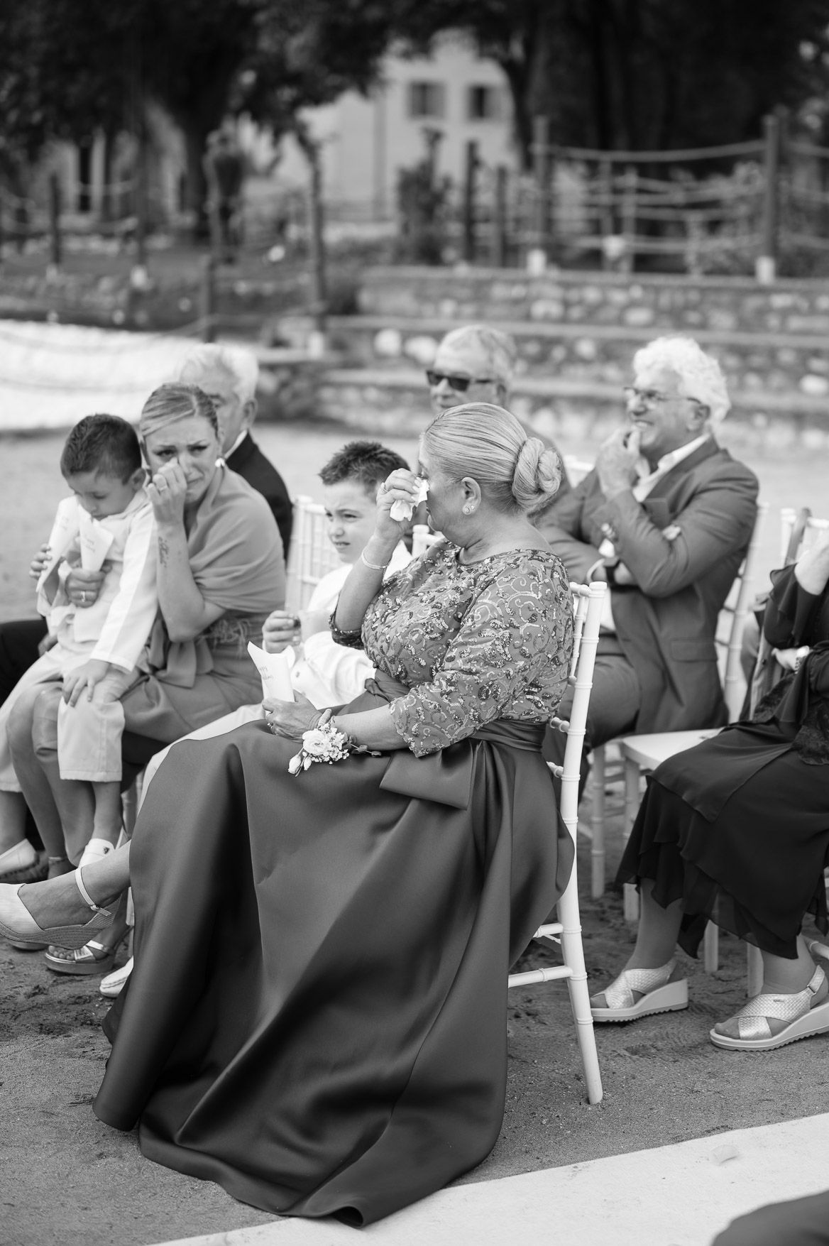 Black and white photo of wedding guests seated in chairs at an outdoor ceremony.