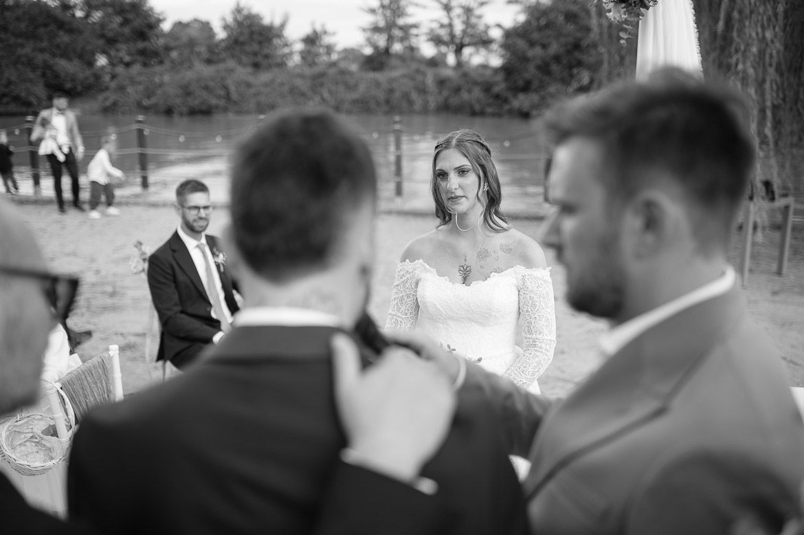 Wedding guests gather outdoors for a celebration under tall trees.