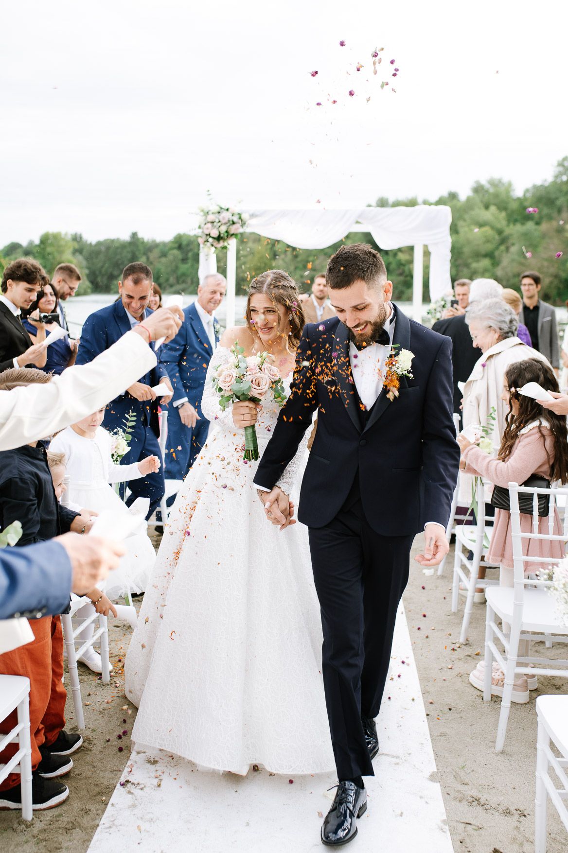 Wedding party celebrates with confetti toss during outdoor ceremony exit.