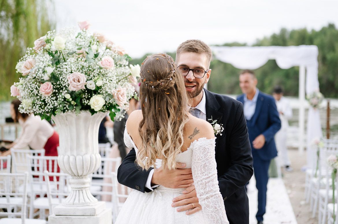 Outdoor wedding ceremony setup with white chairs and floral arrangements under cloudy skies.