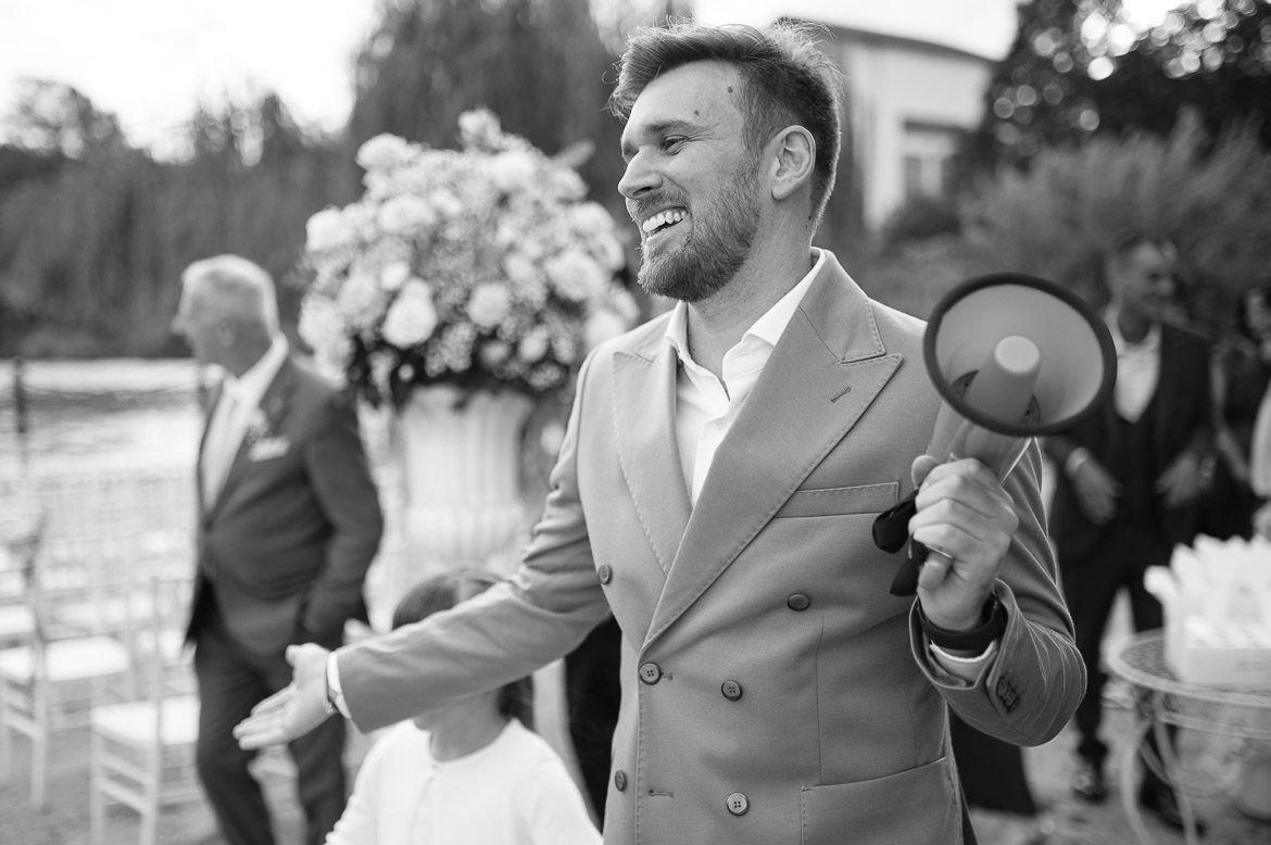 Wedding officiant holding a megaphone and gesturing enthusiastically during an outdoor ceremony.