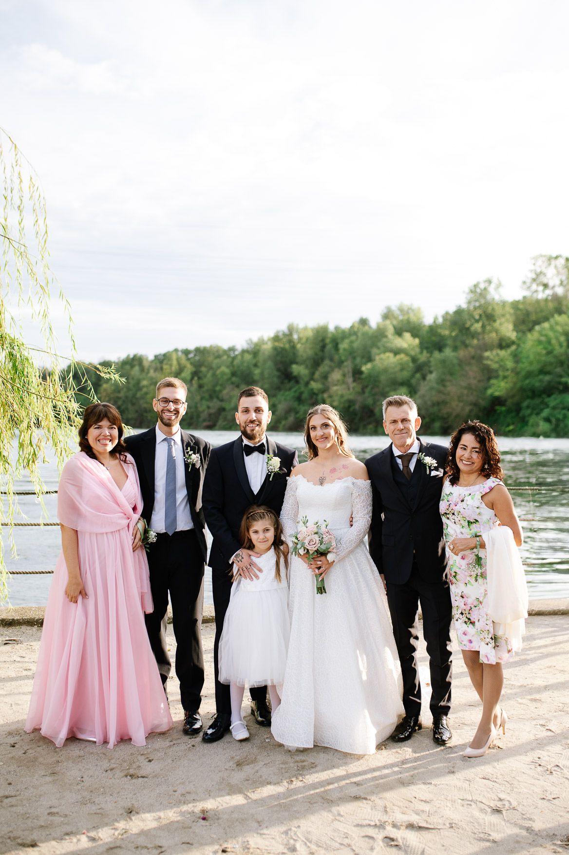 Wedding party poses together on sandy beach with pink bridesmaid dresses and formal attire.