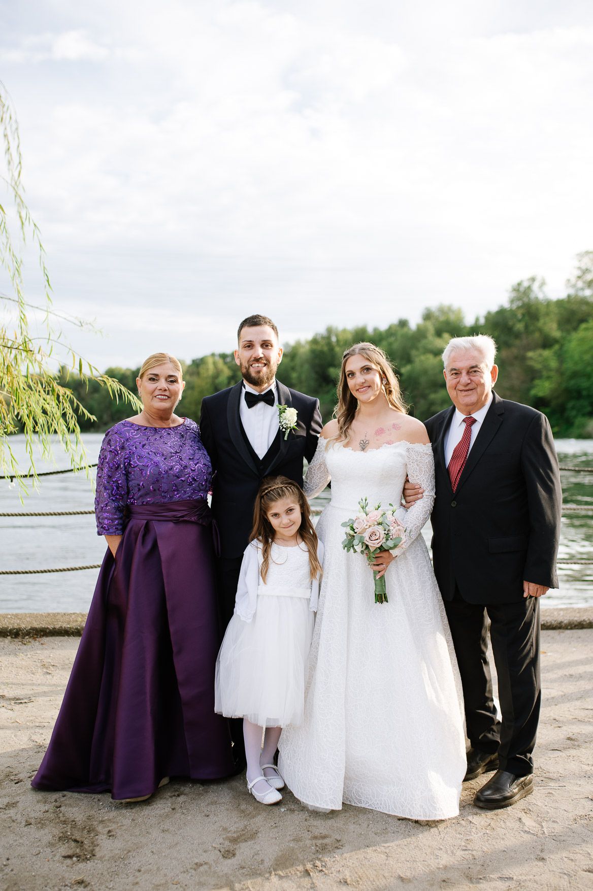 Wedding party members in purple dresses and formal attire pose together outdoors.
