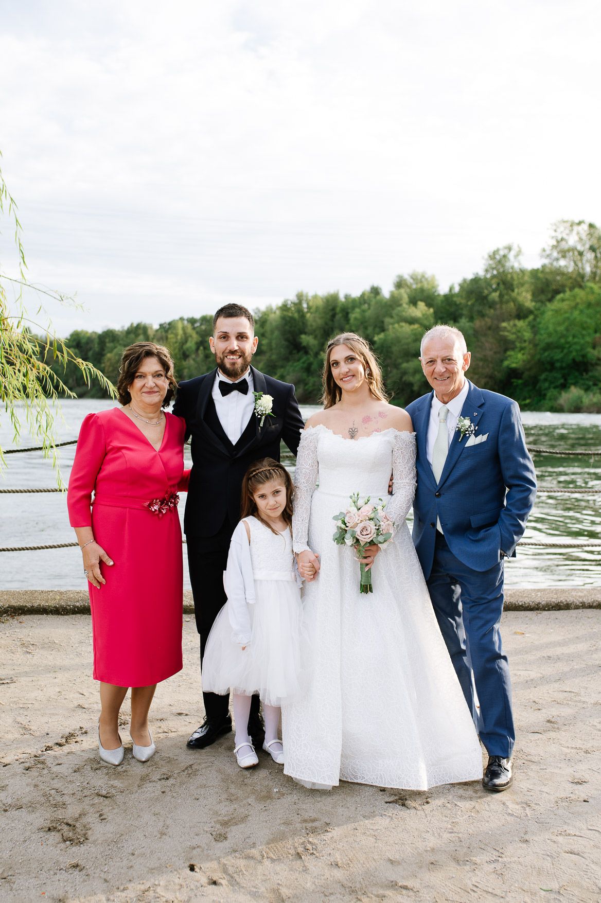 Wedding group photo on beach with bride in white gown and guests in formal wear.
