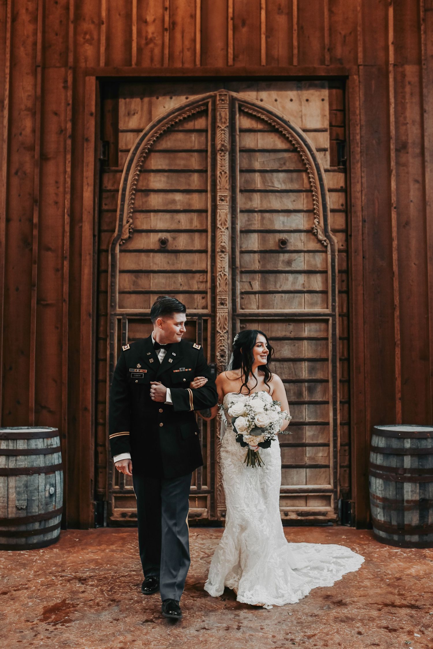 Wide shot of bride and groom in front of the ranch doors highlighting elegant attire and natural textures.