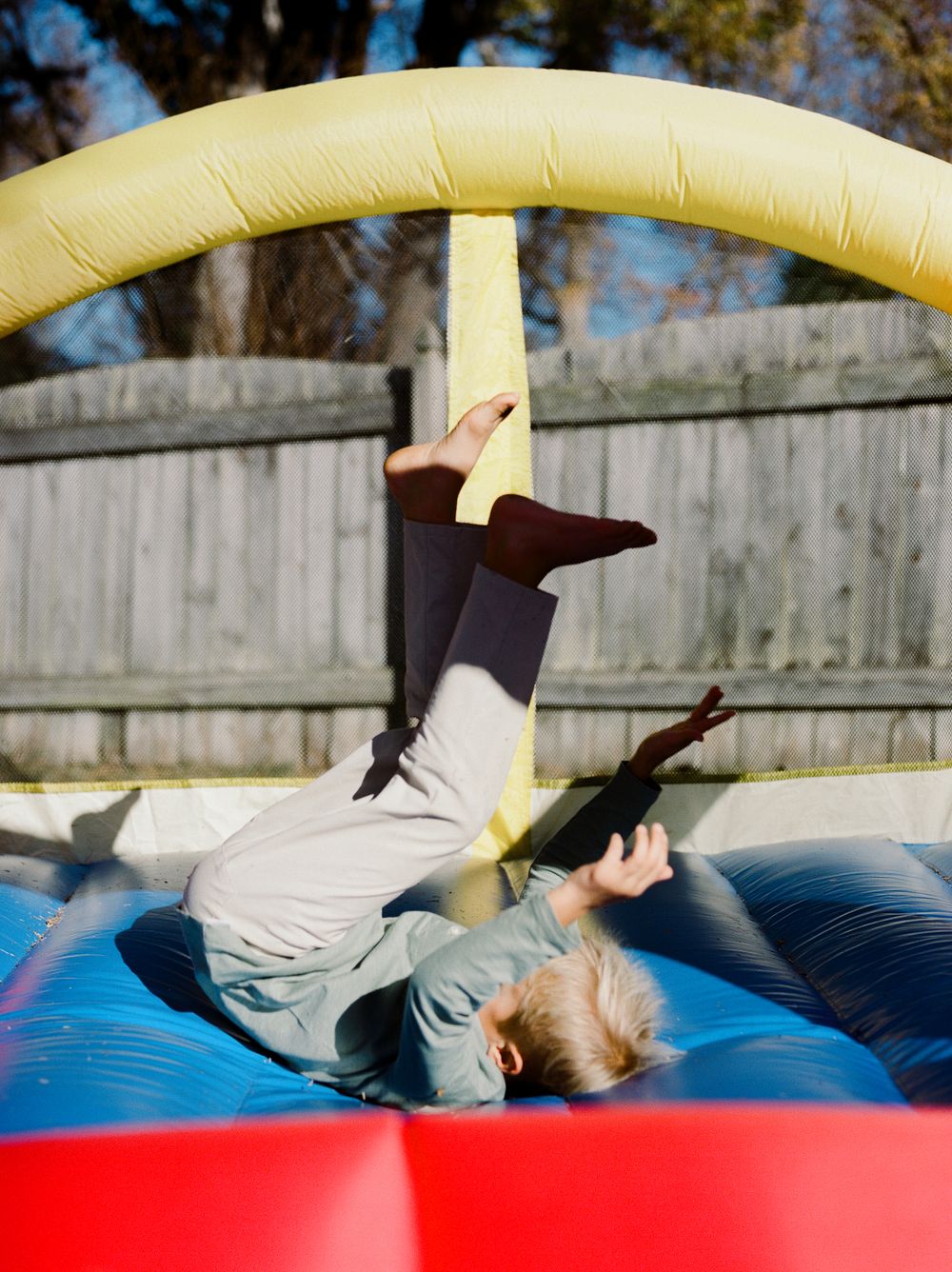 A sequence showing a child tumbling and playing on a blue and red inflatable bounce house outdoors.