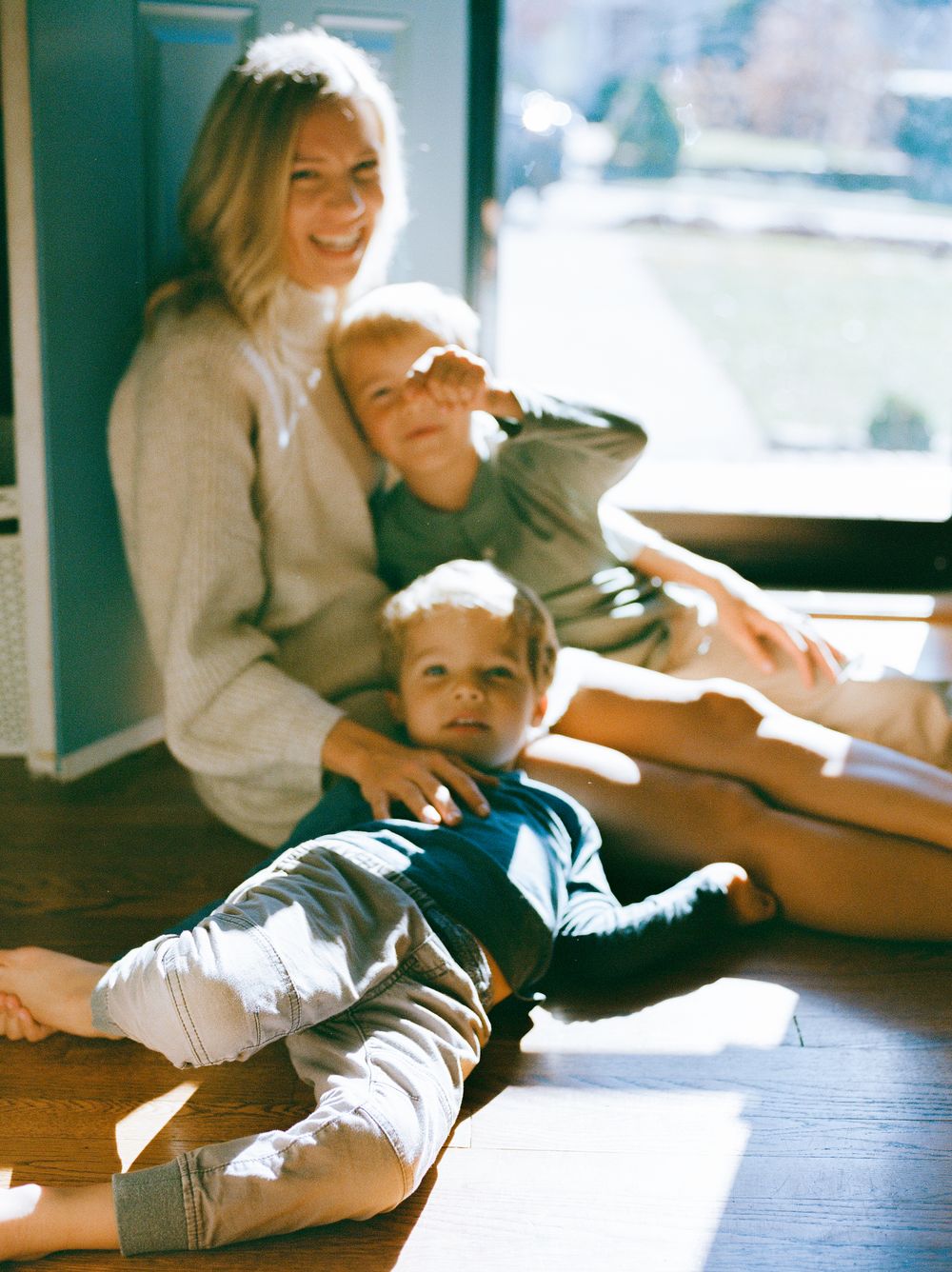 Family relaxing together in sunlit room on wooden floors.
