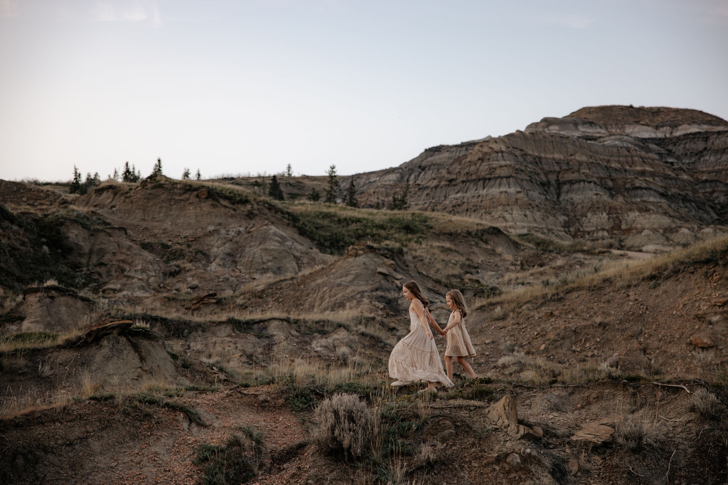 Two girls in dresses stand on dramatic rocky cliffs against a moody sky in alberta during a family photography shoot in alberta