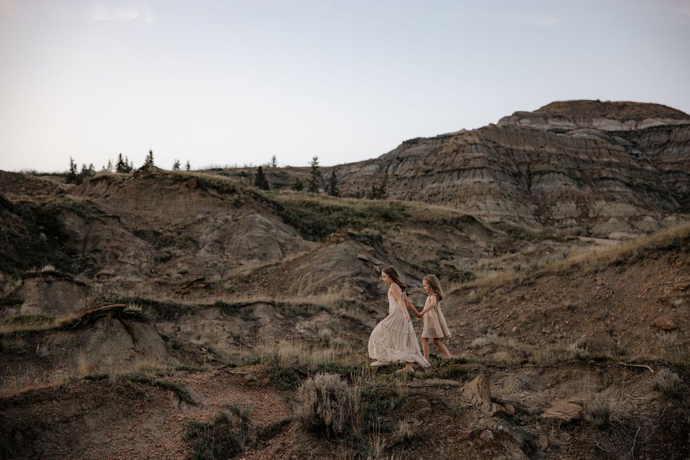 Two girls in dresses stand on dramatic rocky cliffs against a moody sky in alberta during a family photography shoot in alberta