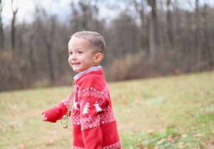 Child wearing festive red sweater smiles during outdoor winter photo session.