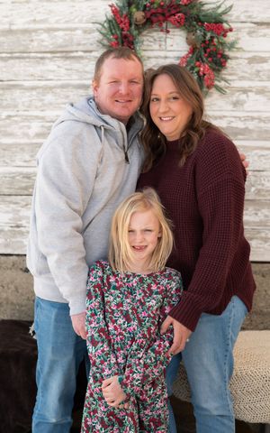 Holiday family portrait against rustic white wood wall with festive evergreen and berry wreath decor.