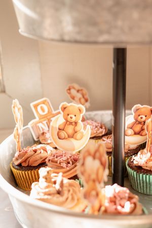 Decorated cupcakes with teddy bear toppers displayed on tiered serving stand.