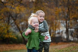 Child in green outfit playing outdoors during fall season.