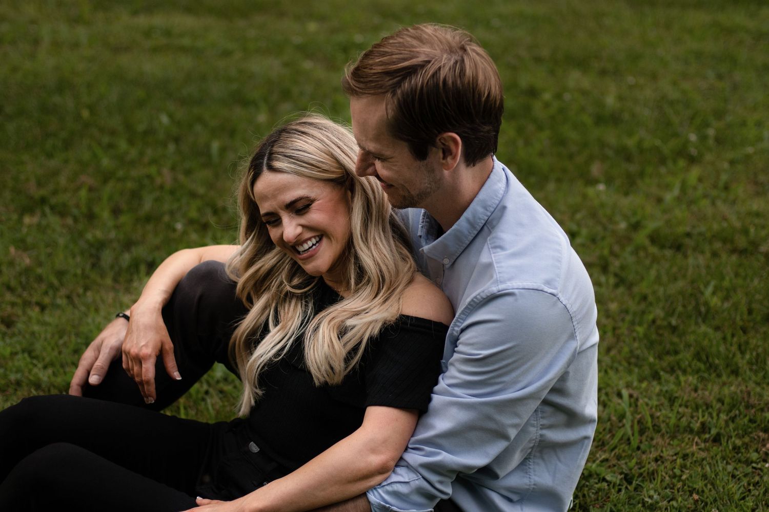 A couple shares an intimate moment while sitting together on grass.
