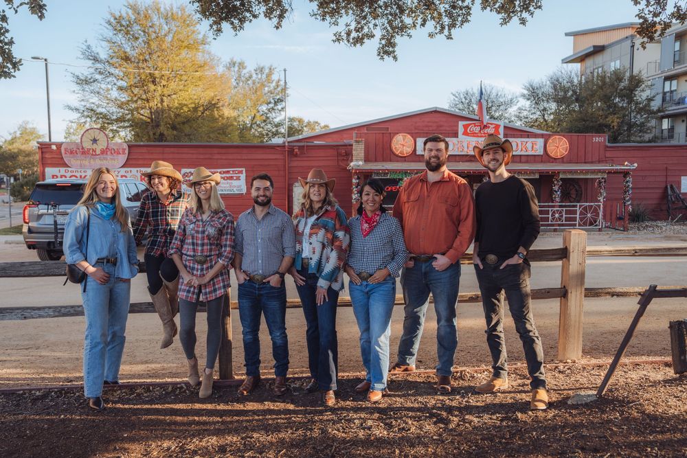 A group of people standing together outside a rustic red building on a sunny autumn day.