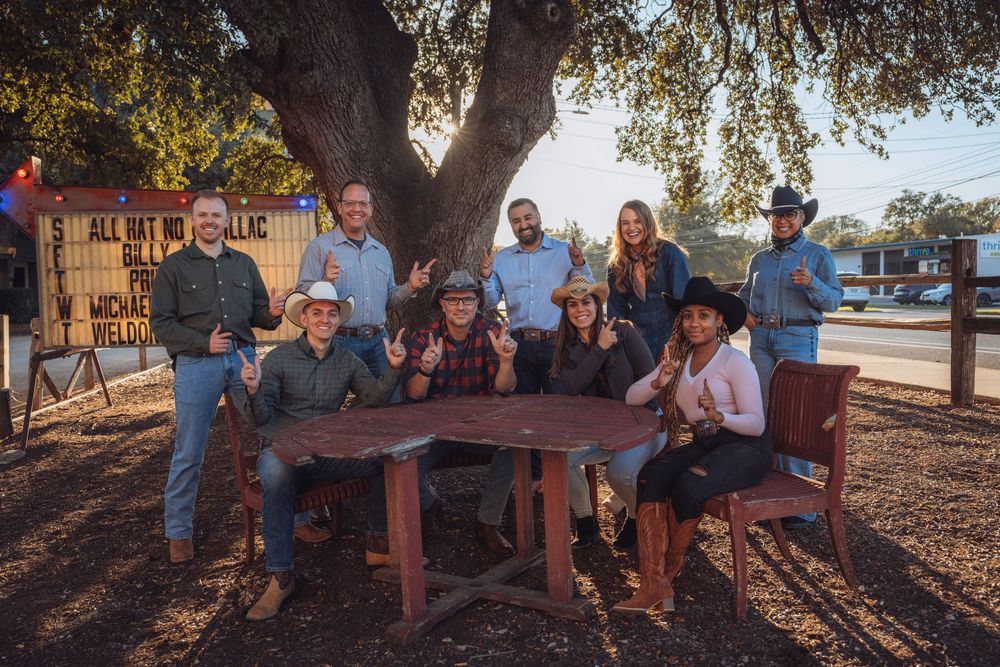 A group of people sit together on a wooden bench in a park during golden hour sunlight.