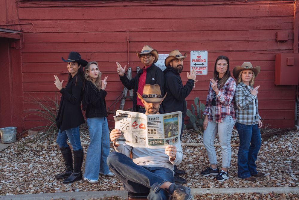 A group poses together against a rustic red barn wall during an outdoor photo session.